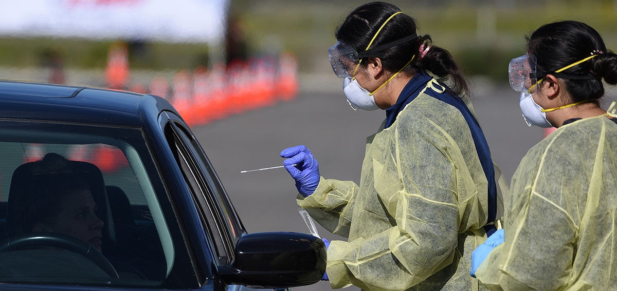 Medical personnel administer COVID-19 swab test at drive-through testing station.