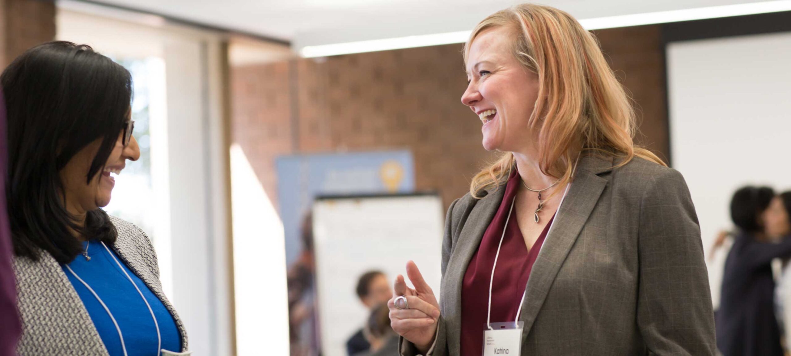 Two women talking an laughing in a meeting setting.