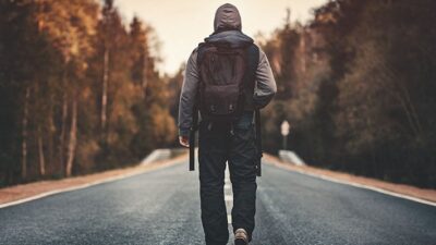 Man carrying backpack walking on road towards sunrise