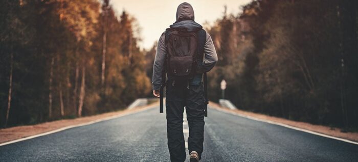Man carrying backpack walking on road towards sunrise