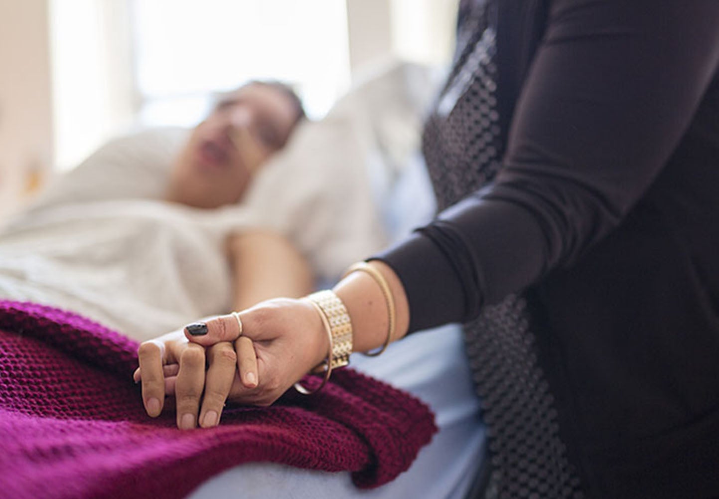 Care-giver holding the hand of patient in bed, receiving palliatve care