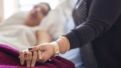 Care-giver holding the hand of patient in bed, receiving palliatve care
