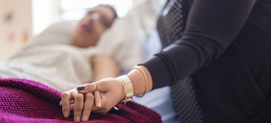 Care-giver holding the hand of patient in bed, receiving palliatve care