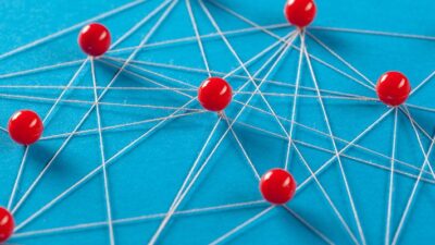 Red push pins and string create a network pattern on a bright blue background.