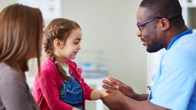 provider wearing scrubs looks at the hand of little girl during a medical exam.