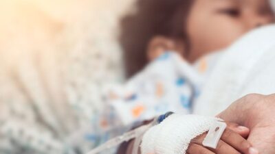 Small child recieving IV infusion with their parent holding their hand.