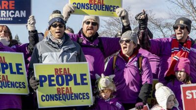 Demonstrators holding signs protesting 2019 government shutdown.