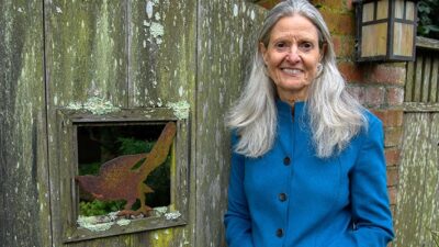 Katy Butler standing by fence with bird sculpture.