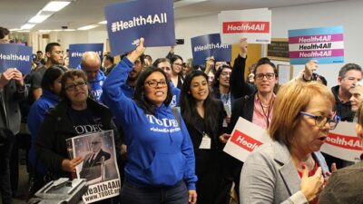 A crowd gathers around state Sen. Maria Elena Durazo before a committee hearing on legislation that would expand Medicaid coverage to adults who are in the country illegally. (Harriet Blair Rowan/California Healthline)