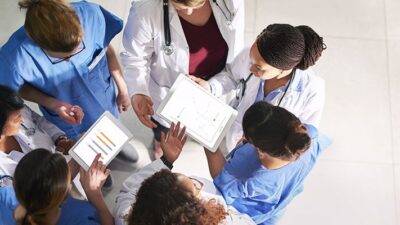 A group of medical providers stand in a circle, digital tablets in hand, having a conversation.