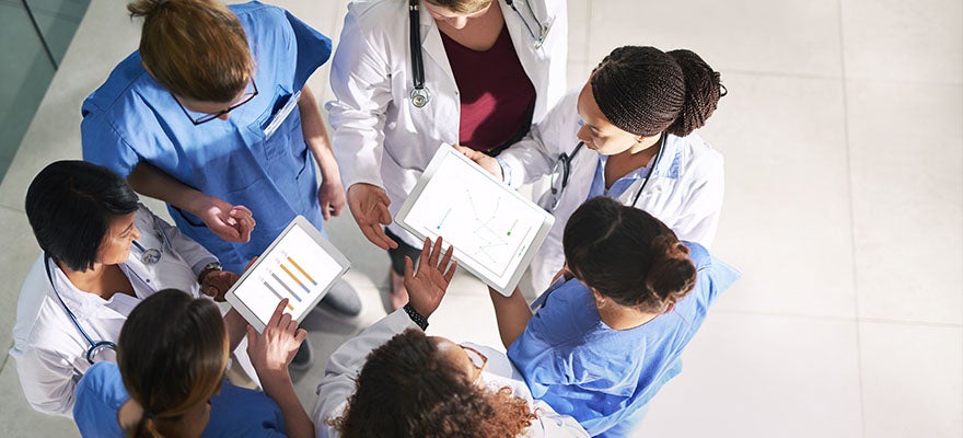 A group of medical providers stand in a circle, digital tablets in hand, having a conversation.