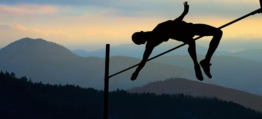 Silouette of pole vaulter clearing the pole.