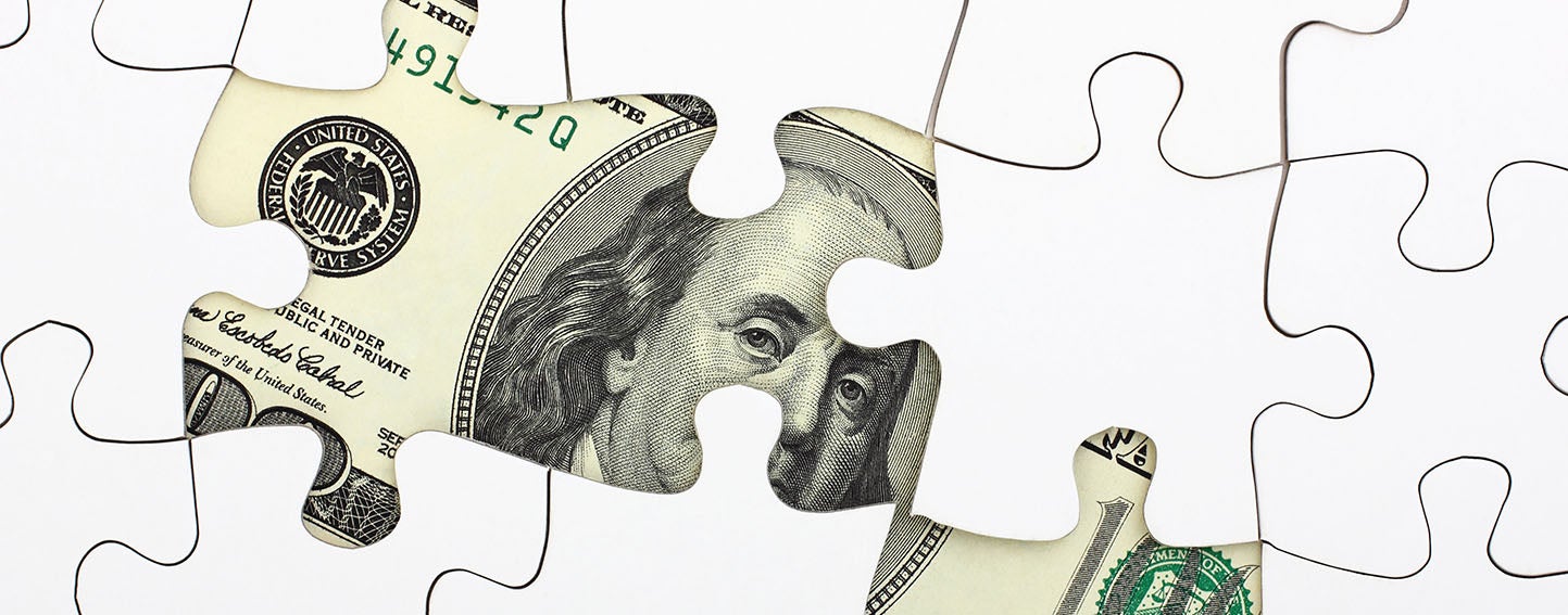 Benjamin Franklin's portrair on a one hundred dollar bill peeks out from underneath a puzzle