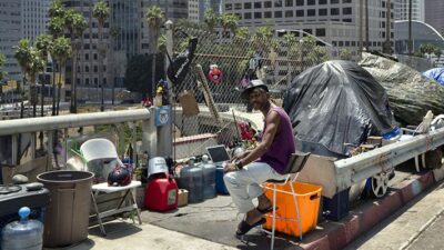 A man sits at his tent in a homeless encampment, along the Interstate 110 freeway in downtown Los Angeles.