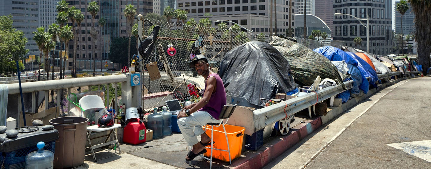 A man sits at his tent in a homeless encampment, along the Interstate 110 freeway in downtown Los Angeles.