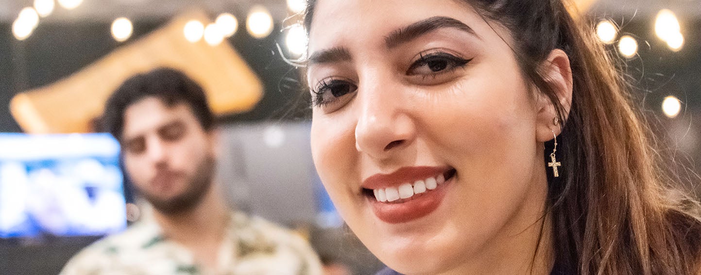 close up-photo of latina woman in mid 20s with man in background