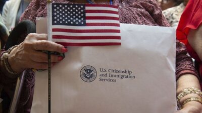 new citizen holds citizenship documents and a flag