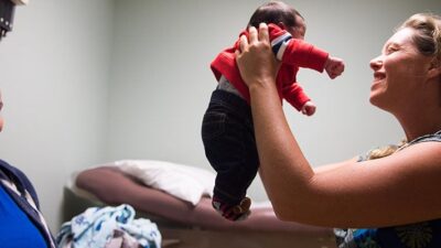 Doctor holds baby while mother looks on, smiling.