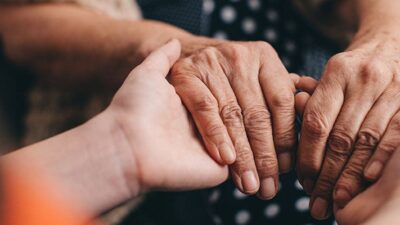 Hands of a younger person holding hands of an older person