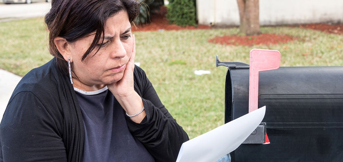 concerned woman reading mail at mailbox