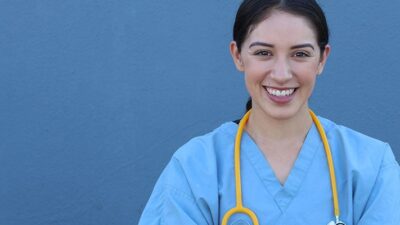 Medical practitioner wearing scrubs stands against a blue wall