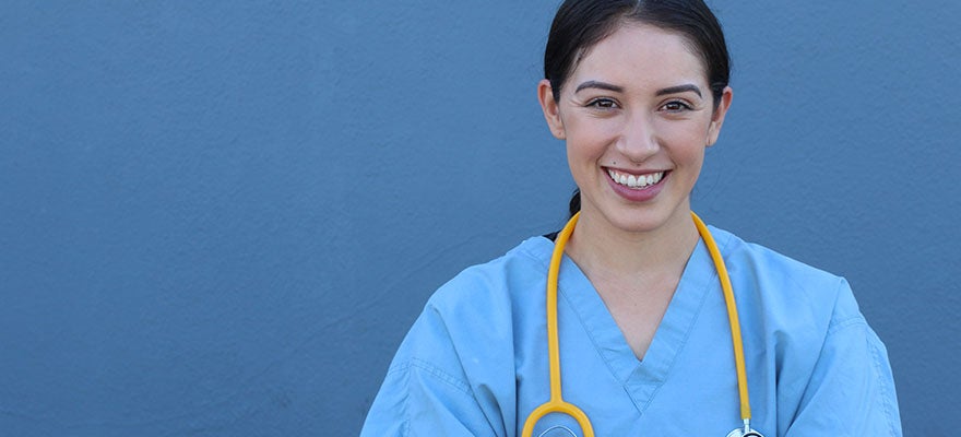 Medical practitioner wearing scrubs stands against a blue wall