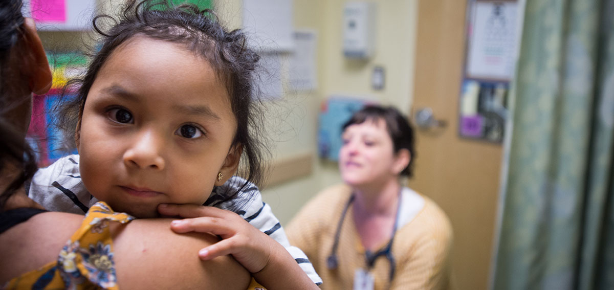 Mother and baby at clinic with doctor. Baby is looking directly into the camera.