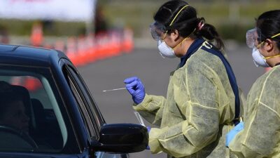 Medical personnel administer COVID-19 swab test at drive-through testing station.