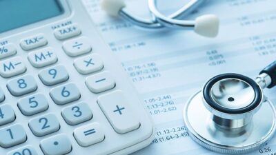 Calculator and stethoscope sitting on a page of medical billing codes.
