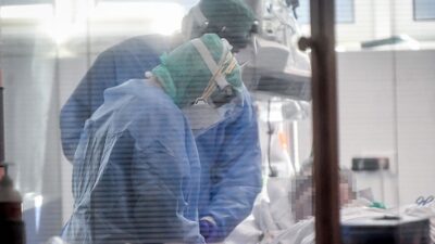 Infectious Disease doctors in full protective gear, tend to elderly patient in Intensive Care Unit.