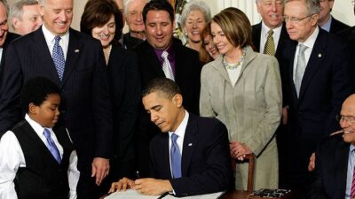 President Obama signing the Affordable Care Act in front of a crowd of legislators and citizens.
