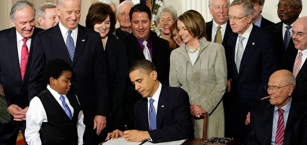 President Obama signing the Affordable Care Act in front of a crowd of legislators and citizens.