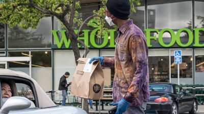 An employee wearing a protective mask hands a shopping bag to a customer outside a Whole Foods Market.