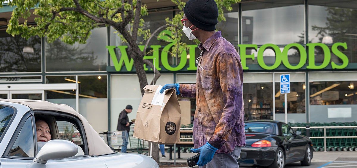 An employee wearing a protective mask hands a shopping bag to a customer outside a Whole Foods Market.