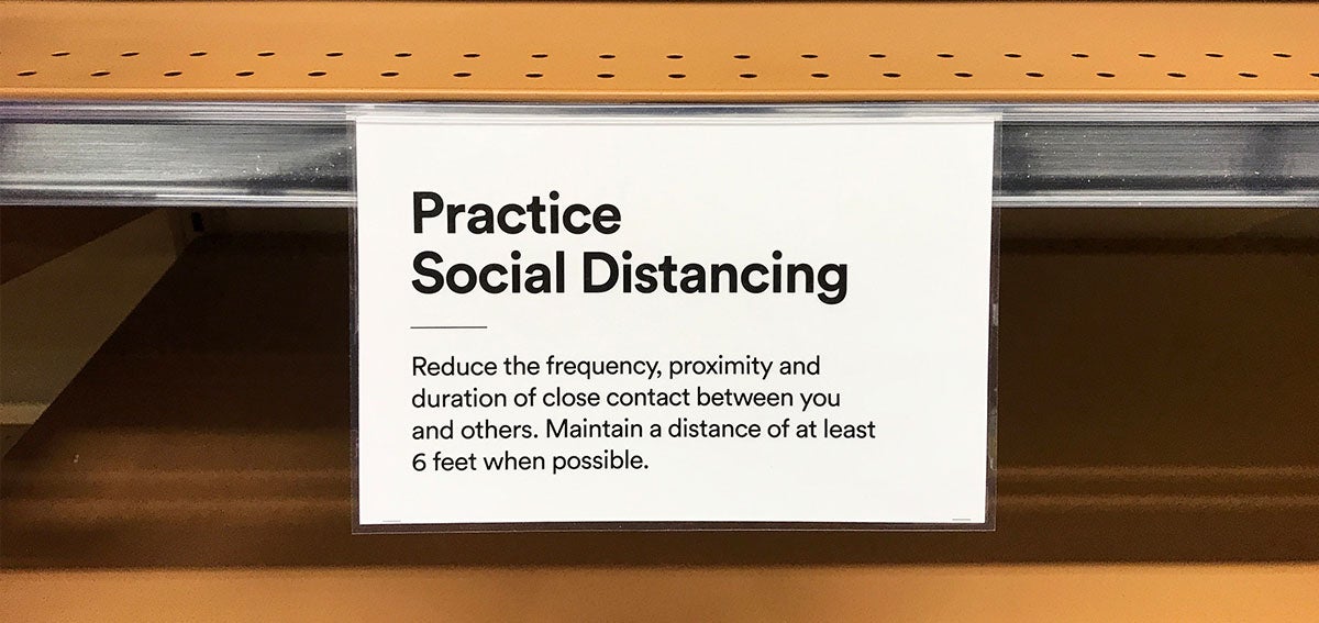 Sign on grocery store shelf reminding customers to practice social distancing