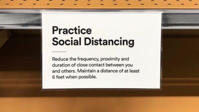 Sign on grocery store shelf reminding customers to practice social distancing