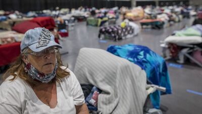 Woman sits on her cot in the Alpha Project area of the San Diego Convention Center