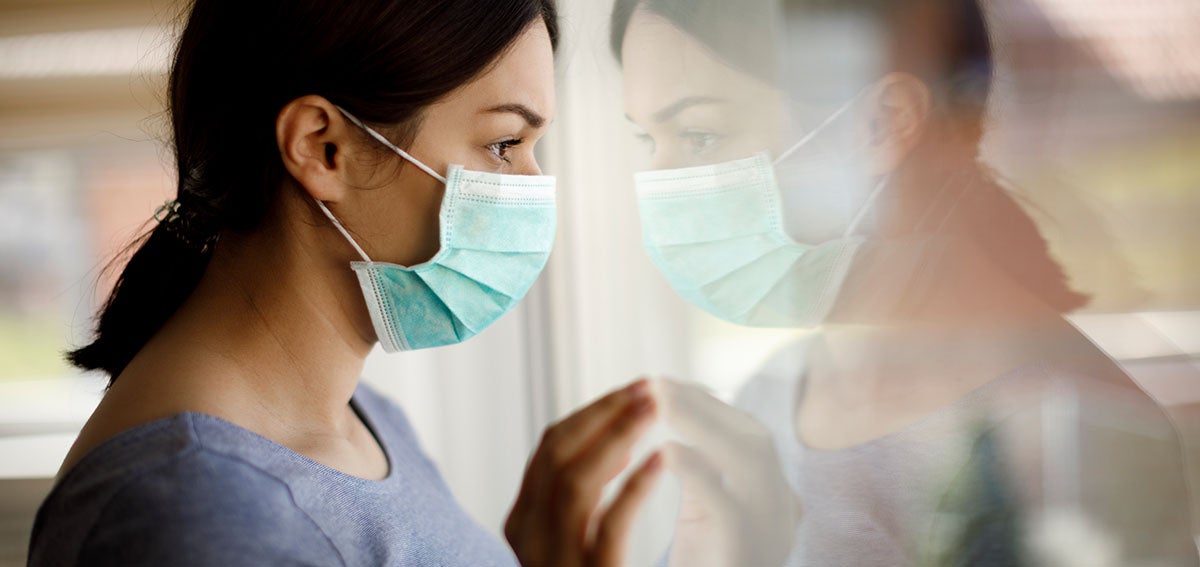 woman wearing surgical mask looking out of window