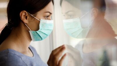 woman wearing surgical mask looking out of window