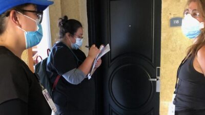 Three health care providers in masks at the door of hotel room.