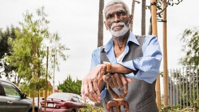 Chris Austin sits outside resting his arms on elaborately carved cane