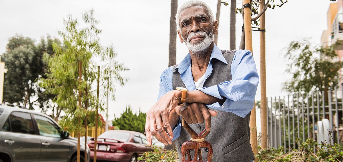 Chris Austin sits outside resting his arms on elaborately carved cane