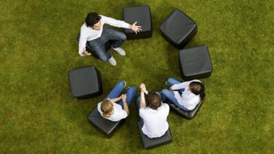 four people sit in a circle on a green lawn having an animated conversation
