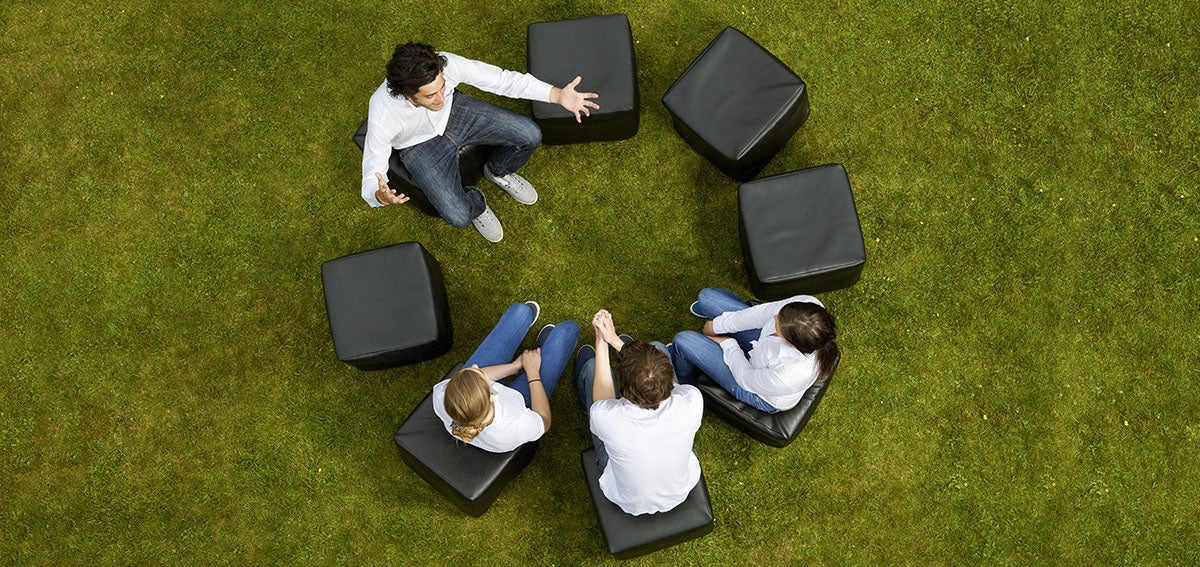 four people sit in a circle on a green lawn having an animated conversation