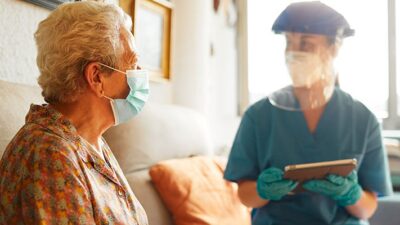 A medical professional wearing PPE speakes to patient in nursing home