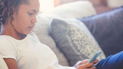 Young girl sitting on sofa using smart phone