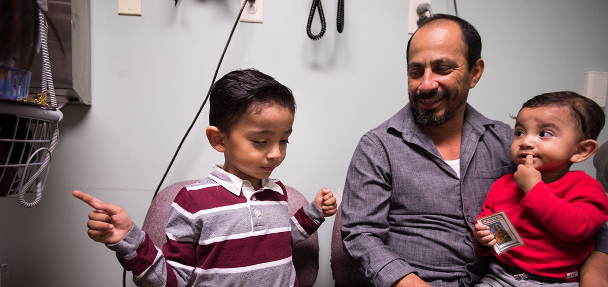 Father and two children sit in clinic exam room.