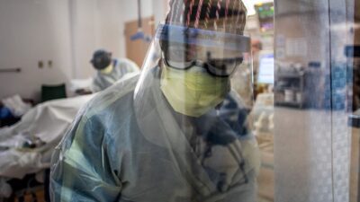 A nurse wearing personal protective equipment (PPE) speaks to a colleagues from inside an Intensive Care Unit (ICU)