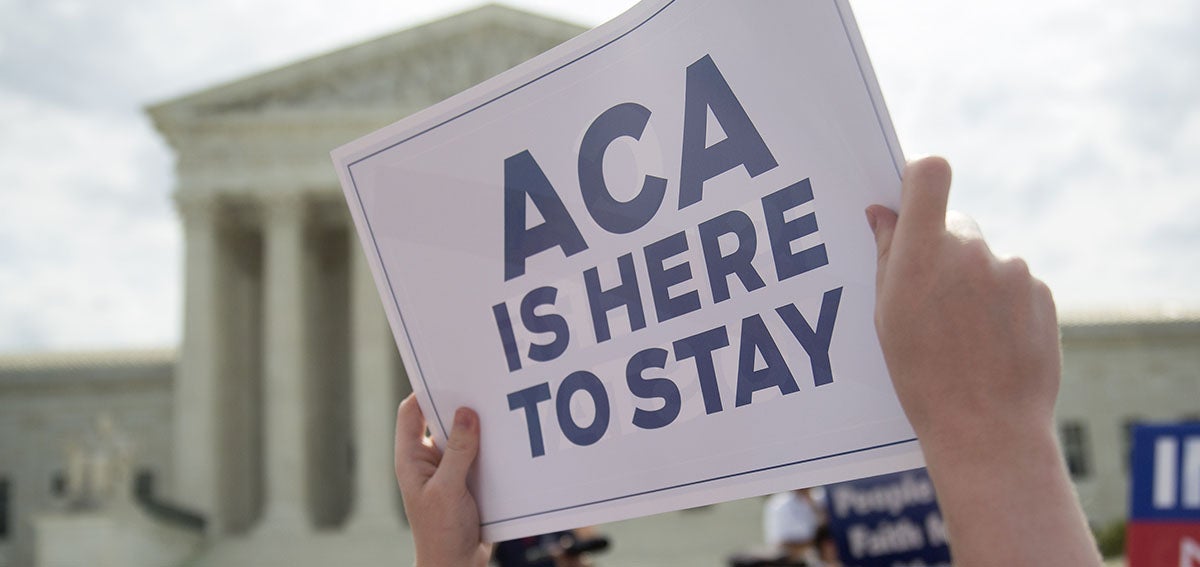 Protestor holds sign that says "ACA is Here to Stay" in front of Supreme Court building