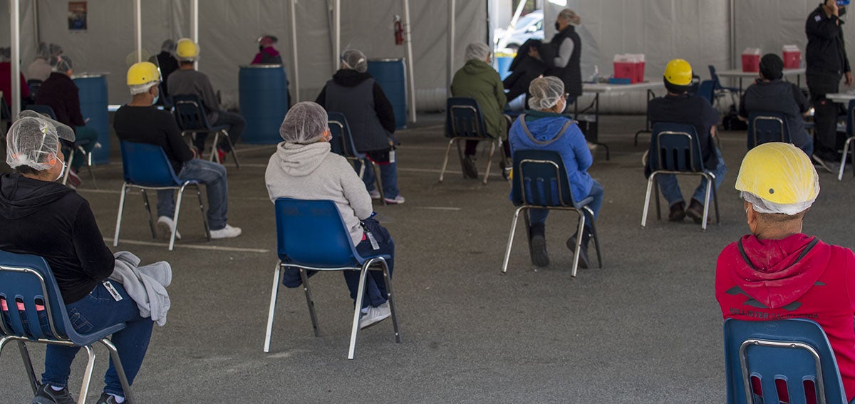 Farmworkers wait after receiving a dose of the Moderna Covid-19 vaccine at a vaccination clinic